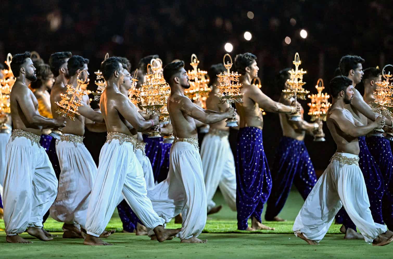Artists carry lamps as they perform at the end of the first innings