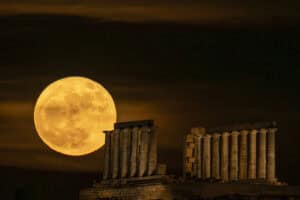 The full moon rises behind the Greek ancient Temple of Poseidon