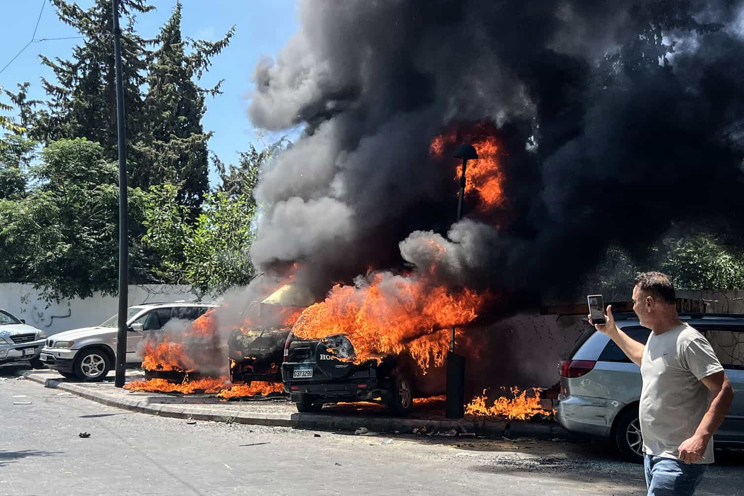 A man takes pictures of burning vehicles following an Israeli airstrike