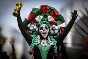 A woman dressed as a Catrina holds up a replica of a World Cup trophy