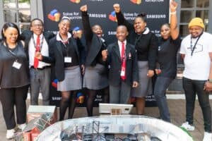 A group celebrates in front of a Samsung Solve for Tomorrow backdrop, standing behind a student-built innovation project.