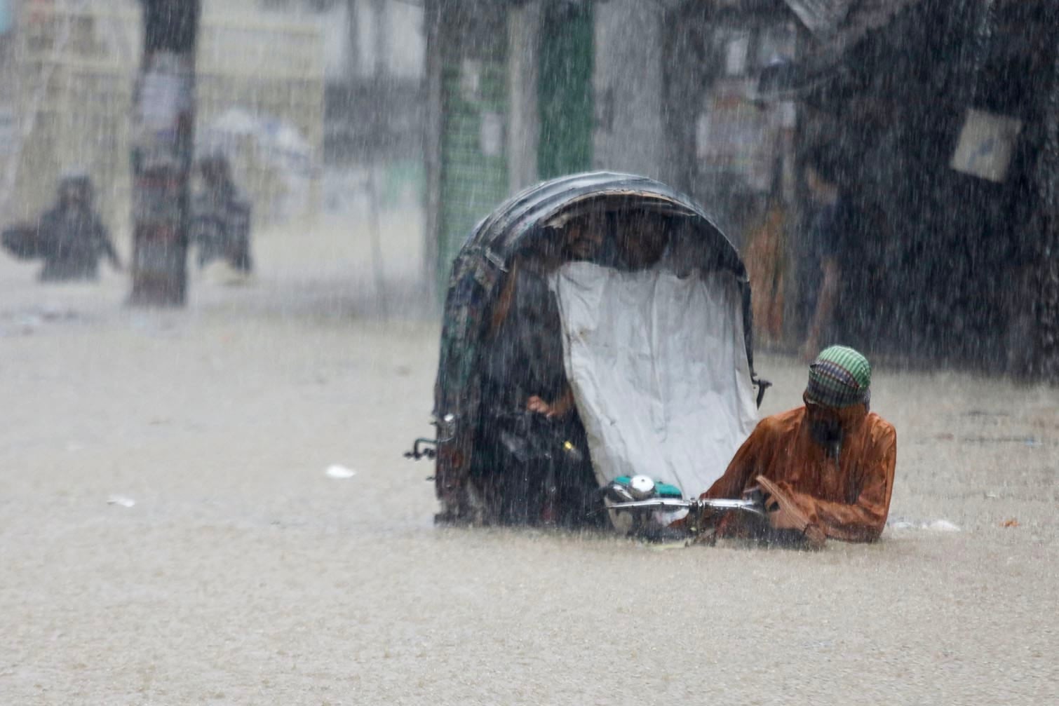 A rickshaw puller wades through a flooded street