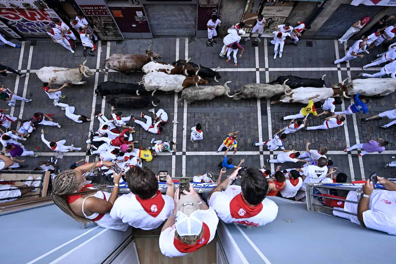 People watch from a balcony as participants run ahead of bulls