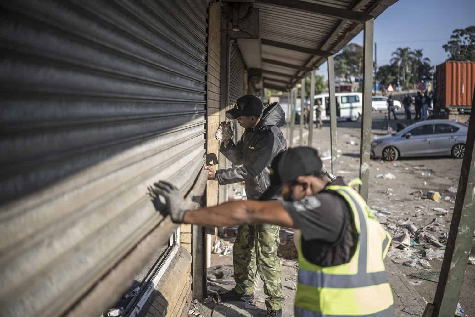 Workers try to dislodge a rolling shutter of a shop looted overnight
