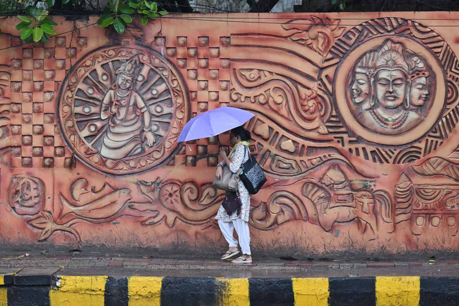 A woman holds an umbrella as she walks past a mural