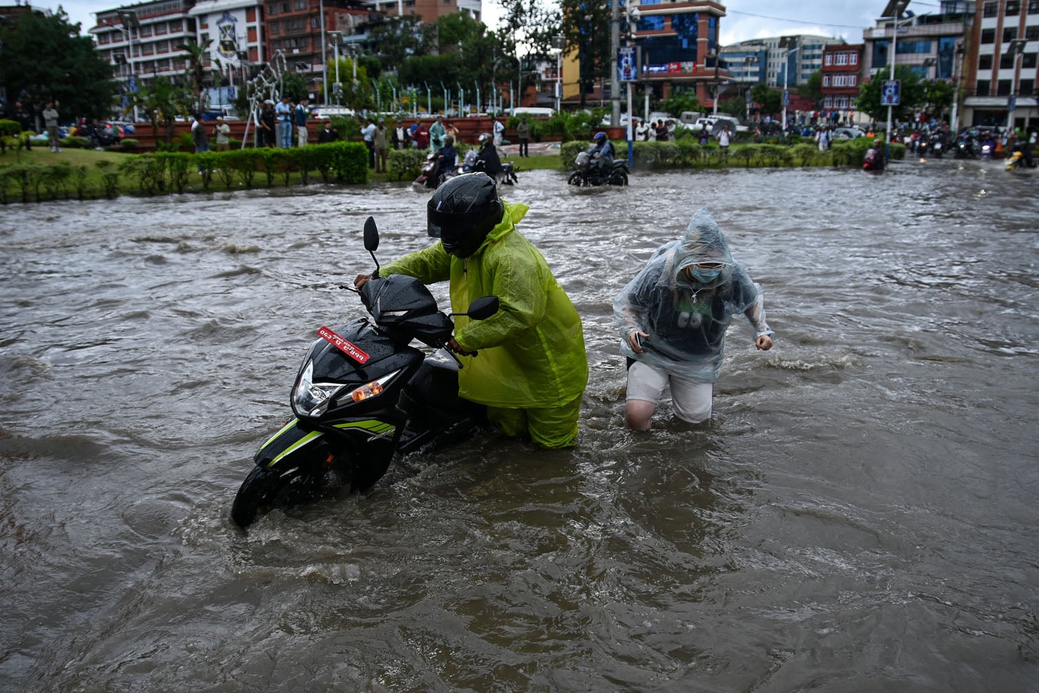 Commuters walking with a scooter wade through a flooded road