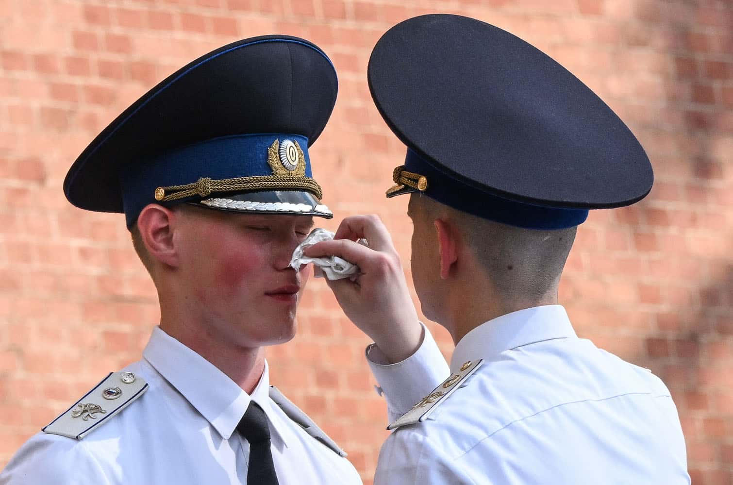 An honor guard serviceman wipes the sweat from his comrade's face