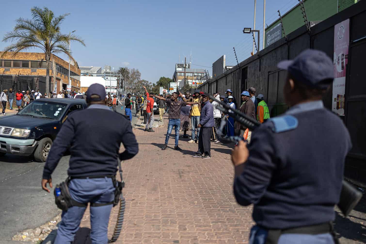 Protesters react as South African Police Service (SAPS) officers threaten to disperse them with rubber bullets during a demonstration calling for the removal of undocumented immigrants in Alexandra township on July 30, 2026. South African President Cyril Ramaphosa called on July 27 for African countries to work together to manage migration, as his government faces mounting pressure over attacks on foreign nationals. Ramaphosa's appeal to the Pan-African Parliament follows weeks of anti-migrant protests in South Africa, where xenophobic activists and fringe groups have blamed undocumented migrants from elsewhere in Africa for crime, unemployment and strain on public services. (Photo by EMMANUEL CROSET / AFP)