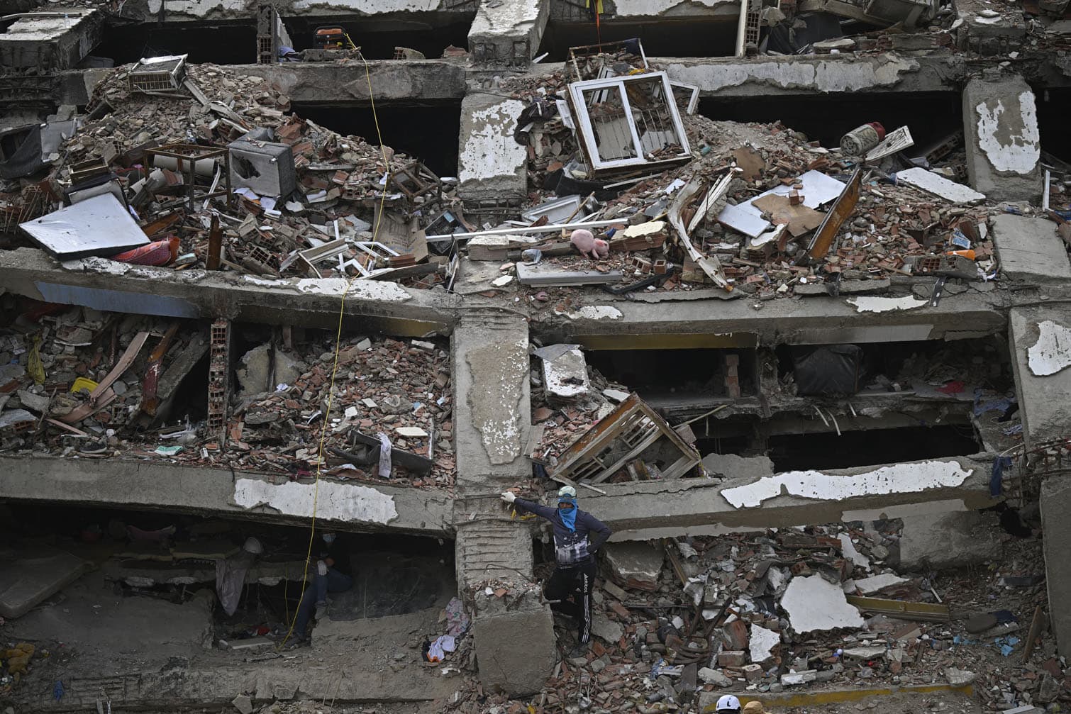 A person stands amid the rubble of a collapsed multi-storey building