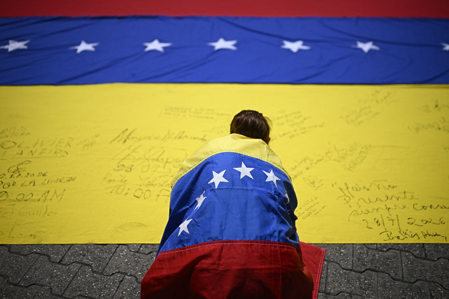 A unionist wrapped in a Venezuelan national flag, signs another Venezuelan national flag during a protest march in demand of elections in Caracas on July 28, 2026. (Photo by Federico PARRA / AFP)