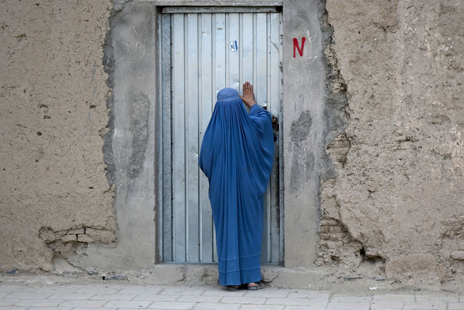 An Afghan burqa-clad woman knocks on a house door in the 6th district of Afghanistan's Kandahar on September 28, 2026. (Photo by Sanaullah SEIAM / AFP)