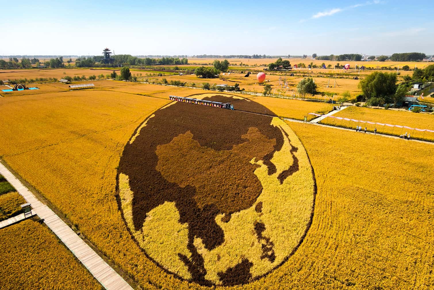 Visitors ride a sight-seeing train (top) past a rice paddy grown in the shape of a map of China, using different coloured rice varieties, at a scenic attraction featuring rice art in Shenyang, in China’s northeast Liaoning province on September 22, 2026. (Photo by CN-STR / AFP)