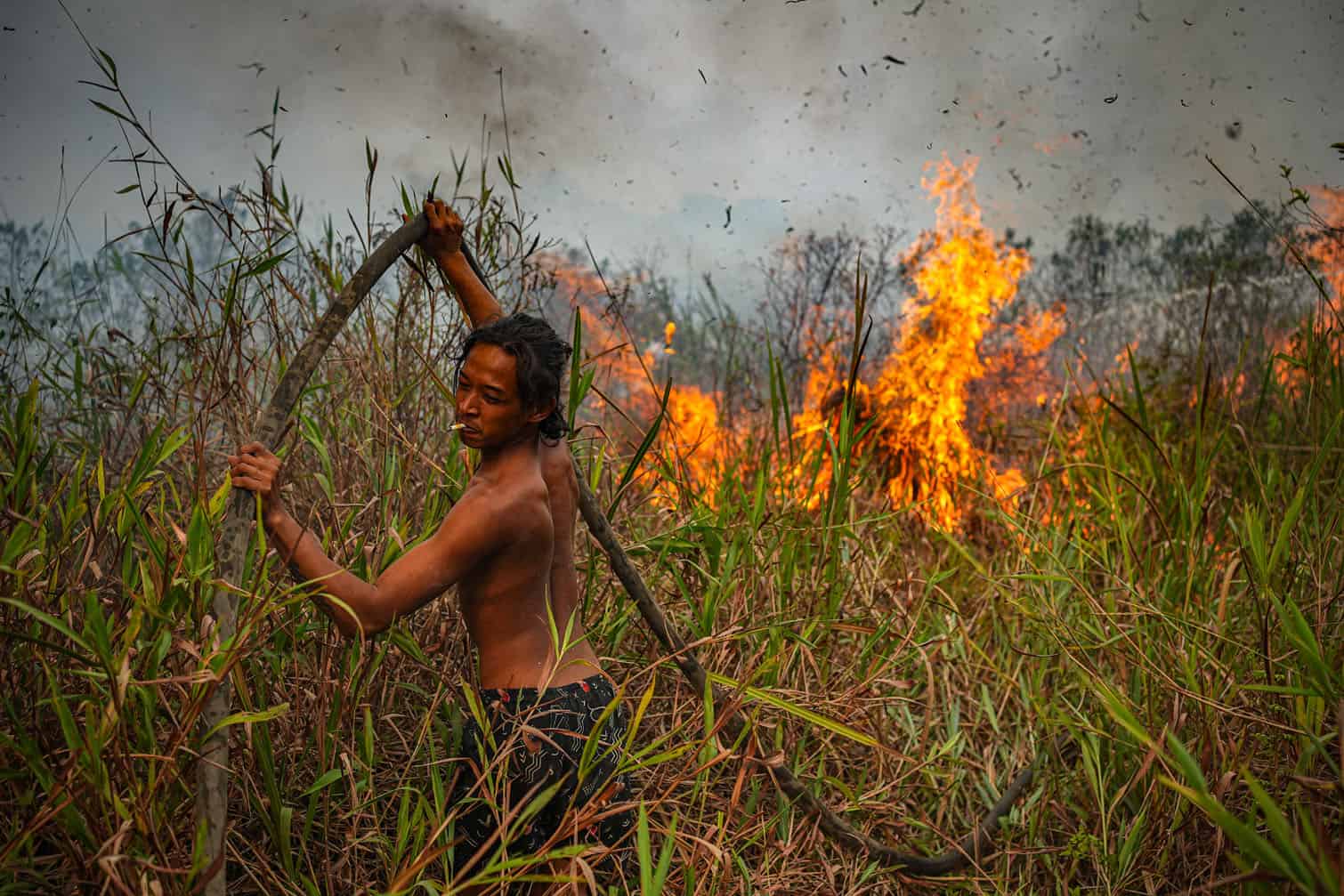 A local resident pulls a fire hose through tall grass and dense peat as he helps battle a raging wildfire in Ogan Ilir, South Sumatra province on September 25, 2026. Low visibility caused by persistent forest fires has hampered both commercial air travel and aerial firefighting operations across the province. (Photo by AL ZULKIFLI / AFP)