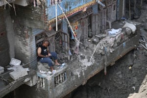 A man sits on the balcony of a sludge-ridden house