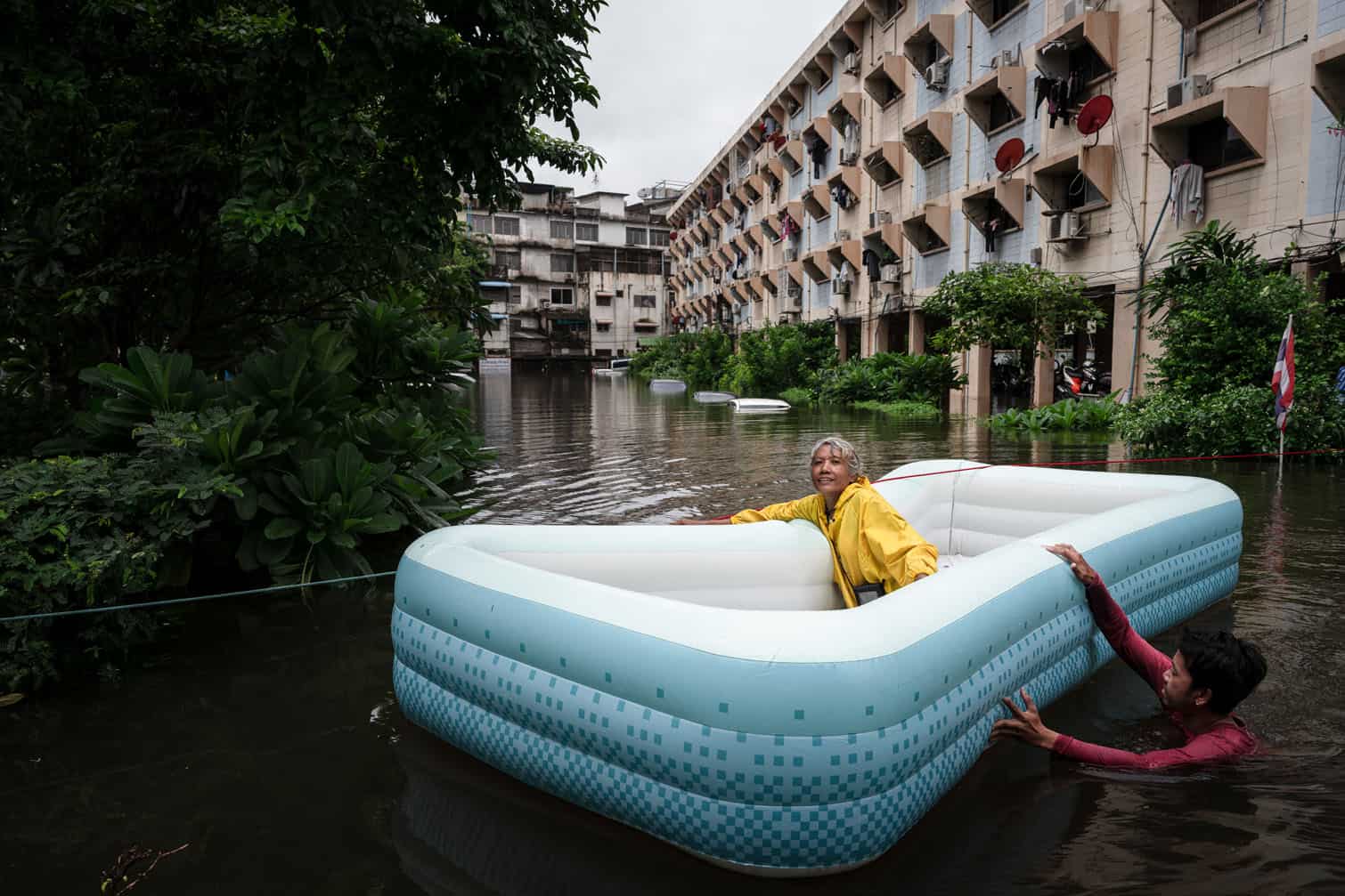A man pulls a woman on an inflatable boat through flood waters in the Bang Kapi district of Bangkok on September 27, 2026. Thousands of Bangkok residents awoke in shelters on September 27 after flooding triggered by days of heavy rain in the Thai capital inundated homes and roads, with some starting to dry out their homes and belongings. (Photo by Chanakarn LAOSARAKHAM / AFP)