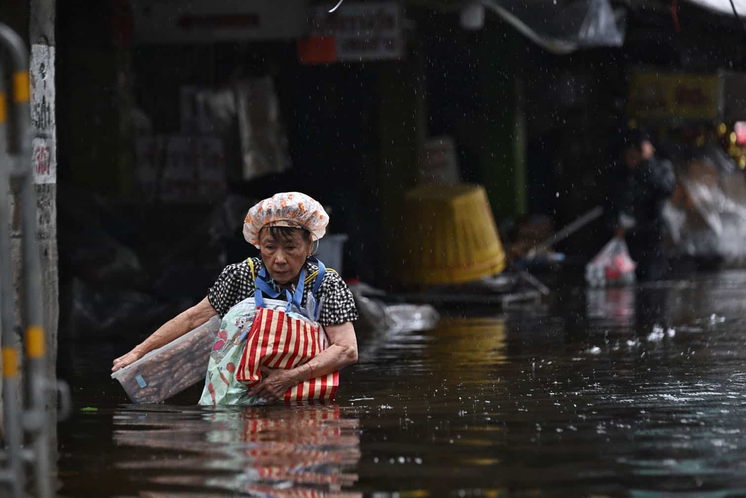 Residents carry supplies while navigating floodwater in Bang Kapi district in Bangkok on September 28, 2026. Eight people have died in flooding in Thailand since September 16, although none in the capital Bangkok which declared a disaster this weekend following heavy rains, the government said on September 28. (Photo by Lillian SUWANRUMPHA / AFP)