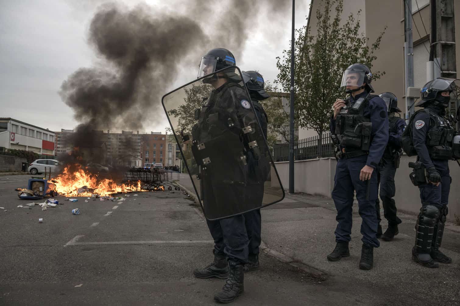 Riot police officers stand guard near burning trash as protesters and high-school students gather outside the Lycee Toulouse Lautrec, in Toulouse on October 12, 2026. Since late September, pupils have barred the entrances to hundreds of schools, complaining of teacher absences, overloaded timetables, dilapidated classrooms and buildings ill-adapted to rising temperatures, among other grievances. (Photo by Ed JONES / AFP)