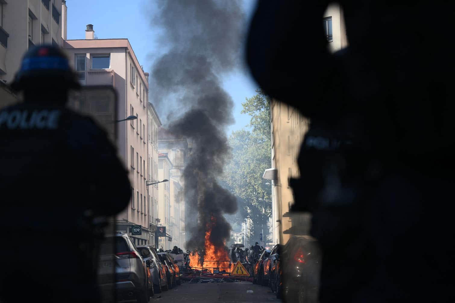 Riot police watch a fire at a makeshift barricade set up by protesters during clashes on the sidelines of a demonstration of high-school students as part of a nationwide protest movement over learning conditions in Lyon, on October 6, 2026. Since late September, pupils have barred the entrances to hundreds of schools, complaining of teacher absences, overloaded timetables, dilapidated classrooms and buildings ill-adapted to rising temperatures, among other grievances. (Photo by Olivier CHASSIGNOLE / AFP)