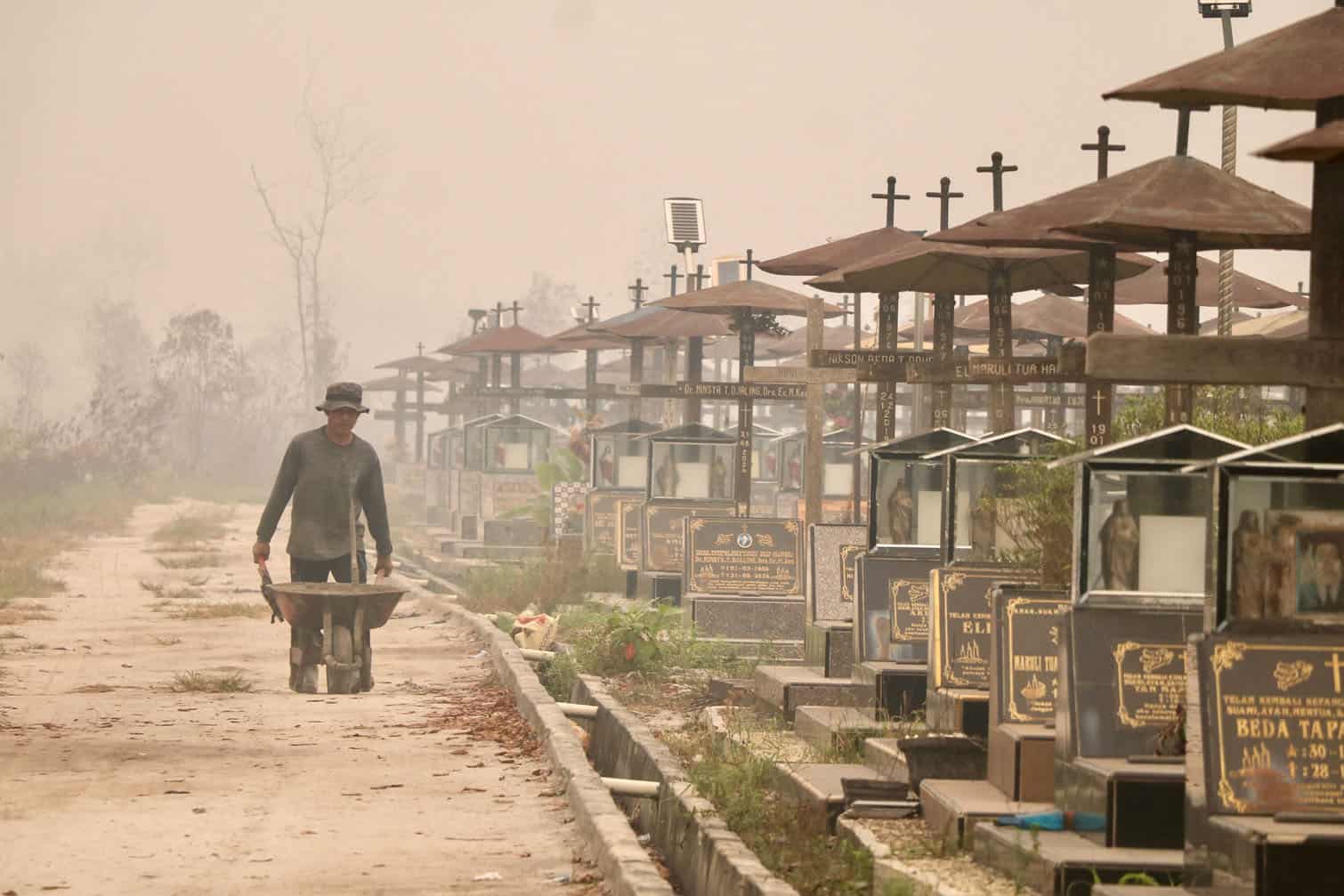 A worker pushes a wheelbarrow through a public cemetery blanketed in thick smoke haze caused by forest and land fires in Palangka Raya, Central Kalimantan province on September 30, 2026. Indonesia has experienced major wildfires, while the warming El Nino weather pattern, which started in June and is due to peak later this year, could drive more fires in southeast Asia. (Photo by REINA / AFP)