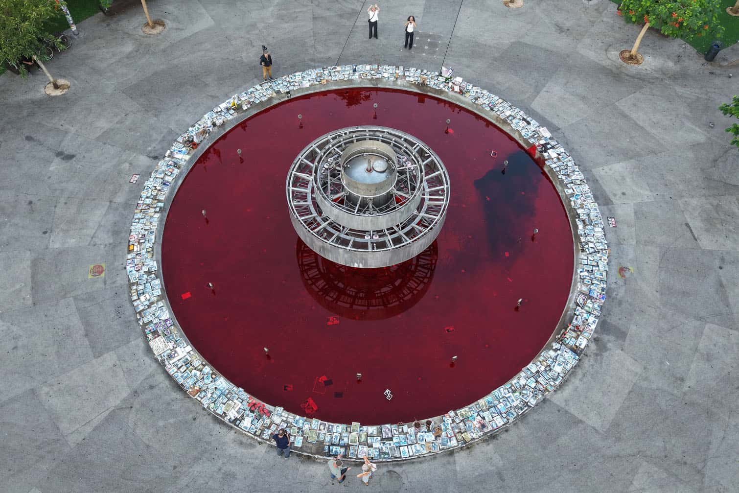 This aerial view shows people standing by the Dizengoff Fountain, filled with red dye in the Israeli coastal city of Tel Aviv on October 7, 2026, to mark the third anniversary of Hamas's October 7 attack. Israel marked the third anniversary of Hamas's October 7 attack with silent tributes, new strikes on Gaza and intense political debate, weeks before elections in which the country's deadliest day will be front and centre. (Photo by Jack GUEZ / AFP)