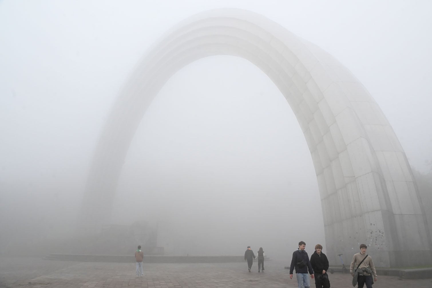 People walk in front of the Arch of Freedom of the Ukrainian People (until May 14, 2022, it was called the Arch of Friendship of Peoples amid heavy fog in Kyiv on October 17, 2026. (Photo by Sergei SUPINSKY / AFP)